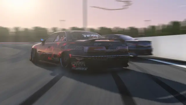 Two cars in a tandem drift past the pit wall at sunset